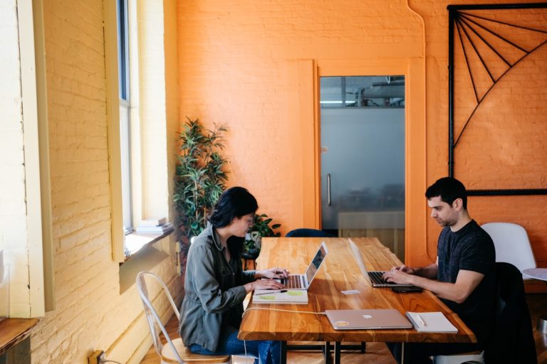 Two individuals working on laptops at a table, discussing the key components of an effective RFP management process.